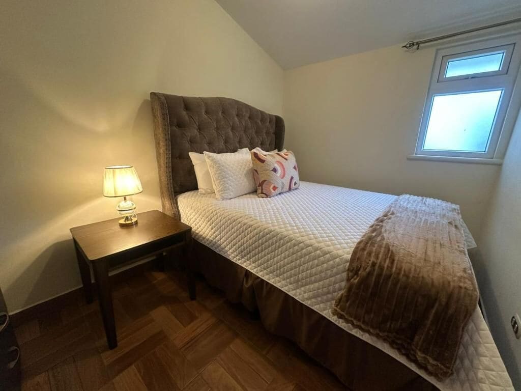 Un dormitorio con cama, mesita de noche, lámpara y ventana.