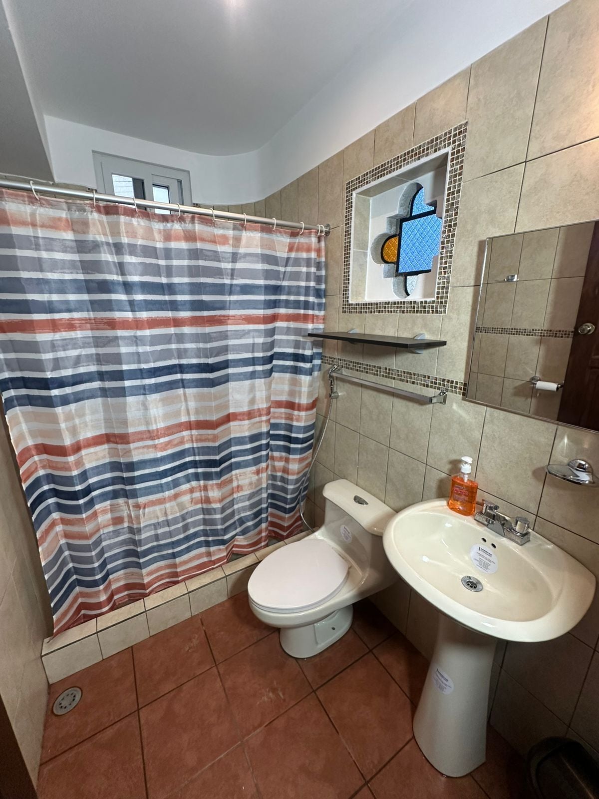 Een badkamer met een gestreepte douchegordijn, toilet, wastafel en spiegel.