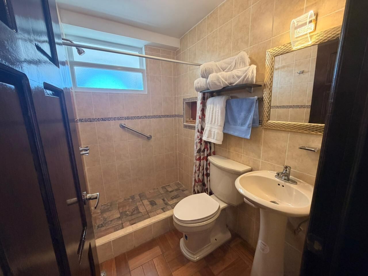 Un baño con ducha, inodoro, lavabo y un perchero para toallas.