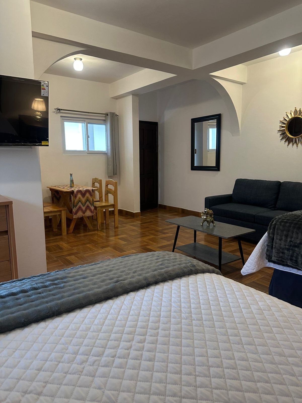 Uma sala de estar moderna com sofá, mesa de centro e televisão. Há uma área de jantar com mesa e cadeiras.
