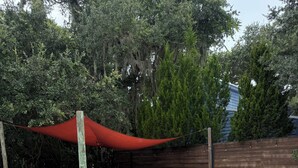 Une piscine rectangulaire dont les bords sont recouverts de carreaux, entourée d’une clôture en bois, et surmontée d’un auvent rouge qui abrite un espace détente.