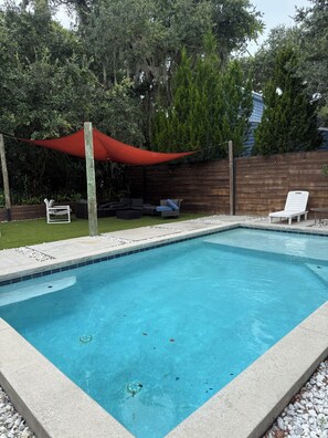 A rectangular swimming pool with a tiled edge, surrounded by a wooden fence, and a red canopy over a seating area. - Beautiful pet friendly three bedroom home with Pool near beach and attraction's (St. Augustine)