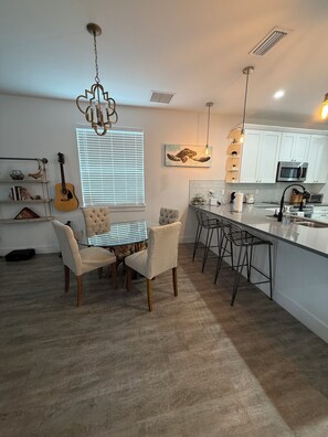 A modern kitchen with white cabinets, a central island, bar stools, and a dining table with chairs. - Beautiful pet friendly three bedroom home with Pool near beach and attraction's (St. Augustine)