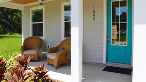 Une maison avec un porche, deux chaises en osier, une porte d’entrée de couleur turquoise et le numéro « 652 » peint sur le mur.