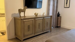 Une chambre à coucher avec un lit, une commode en bois, un téléviseur à écran plat et un tableau encadré au mur.