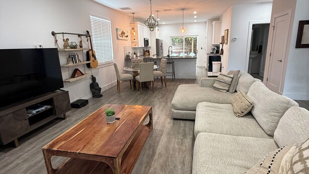 Un salon moderne avec un téléviseur à écran plat, une table basse en bois, un canapé beige et un ventilateur de plafond.