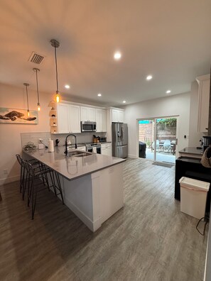 A modern kitchen with white cabinetry, stainless steel appliances, and a central island with bar stools. - Beautiful pet friendly three bedroom home with Pool near beach and attraction's (St. Augustine)