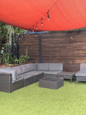 A sectional sofa and a small table in a garden area with a wooden fence and a red canopy. - Beautiful pet friendly three bedroom home with Pool near beach and attraction's (St. Augustine)