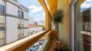 Ein Balkon mit einer Topfpflanze, einem Fenster und Blick auf die Straße darunter.