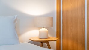 A bed with a white pillow and a round wooden nightstand with a lamp. - T2 Moderno c/Varanda em Portimão by Lovelystay (Portimão)