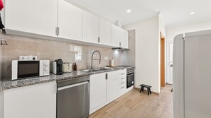 A modern kitchen with white cabinetry, a stainless steel dishwasher, a built-in oven, and a granite countertop. - T2 Moderno c/Varanda em Portimão by Lovelystay (Portimão)