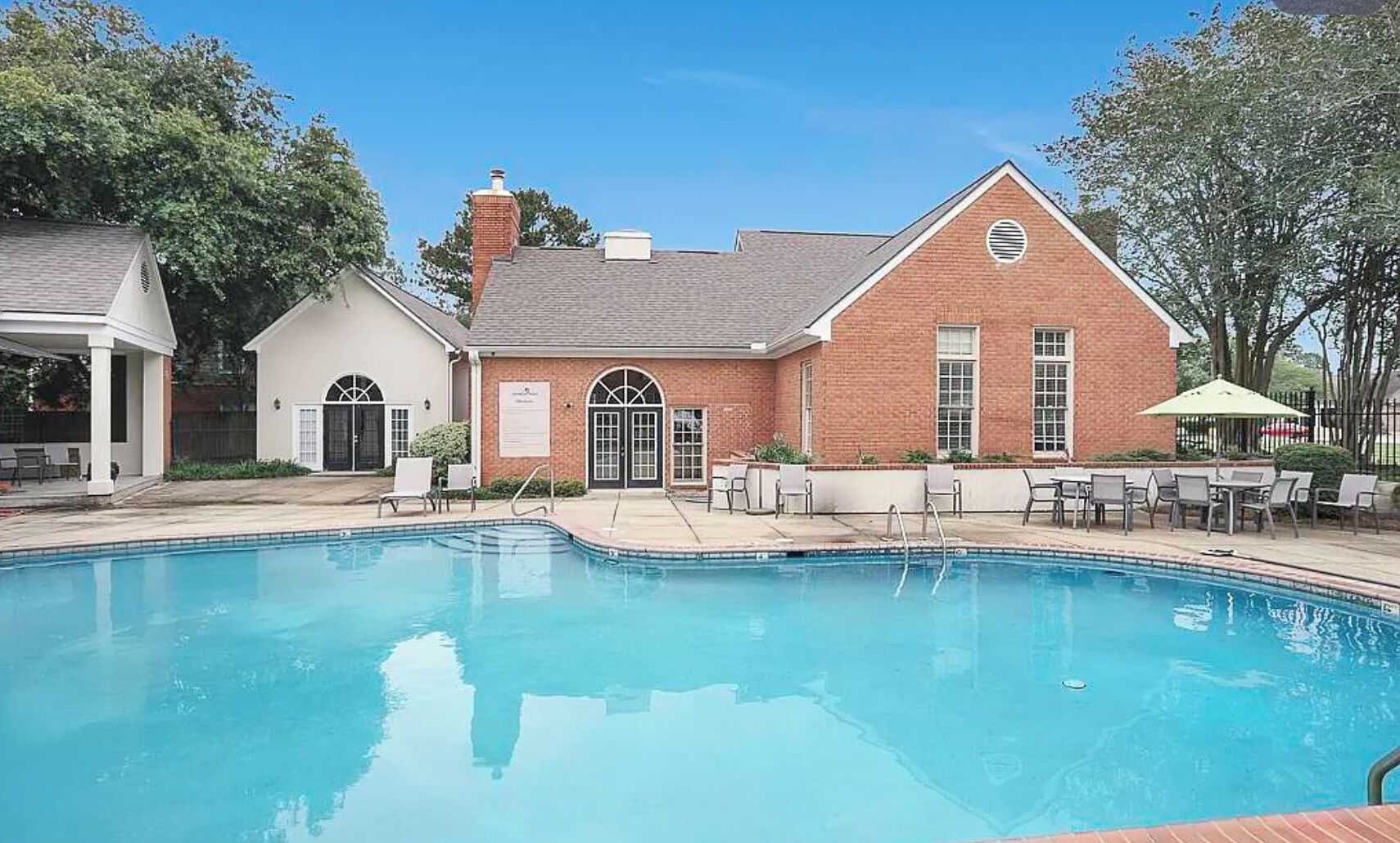A swimming pool with lounge chairs and a building with a brick facade.