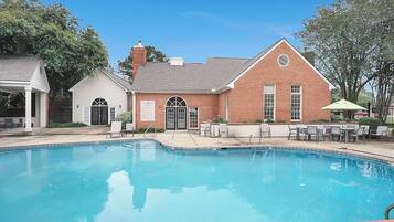 A swimming pool with lounge chairs and a building with a brick facade.