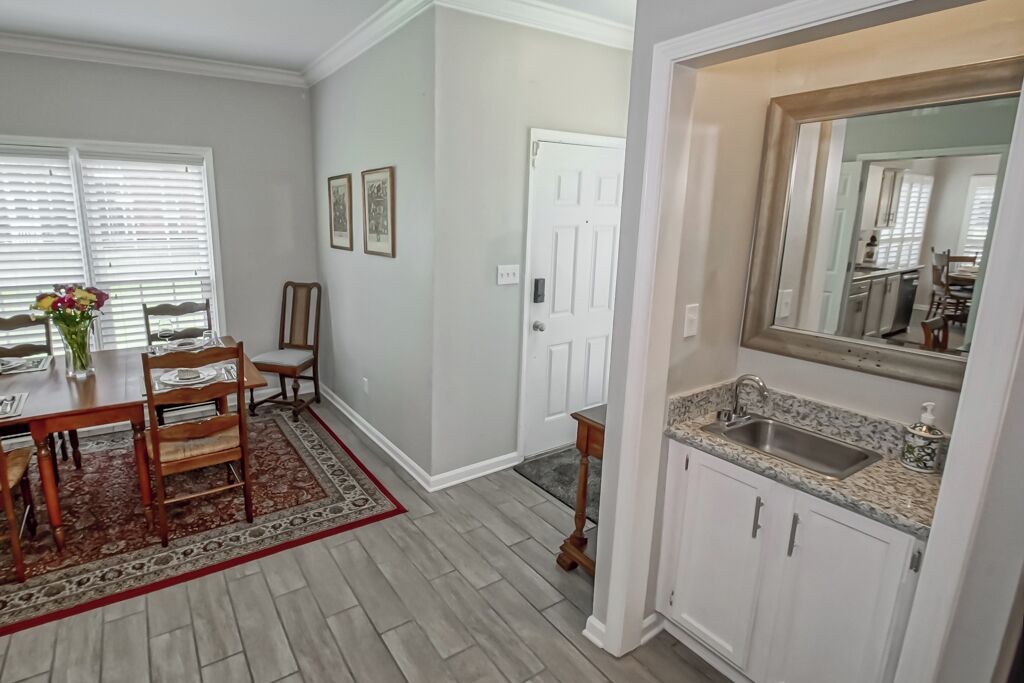 A dining area with a wooden table and chairs, a rug, and a window with blinds.