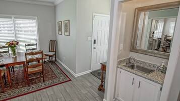 A dining area with a wooden table and chairs, a rug, and a window with blinds.