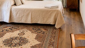Um quarto com uma cama, uma cadeira, uma escrivaninha de madeira e um tapete estampado.