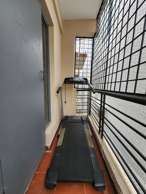 A narrow corridor with a treadmill, a door, and a window with a metal grid. - Modern 2 Bed Apartment near Bannergatta Road. 5 minutes to Apollo Hospital (Bengaluru)