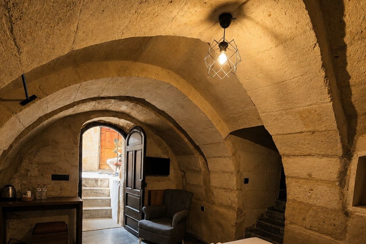 A room with a vaulted ceiling, a bed with a white bedspread, a chair, and a desk with a lamp.