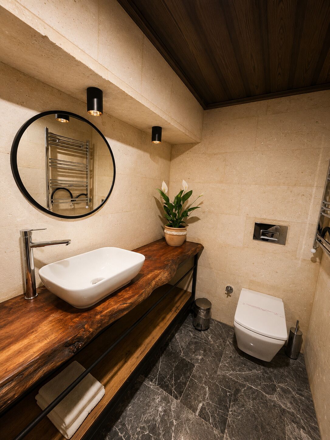 A modern bathroom with a wooden vanity, a round mirror, a white sink, a toilet, and a potted plant.