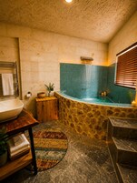 A bathroom with a stone wall, a bathtub, a sink, and a wooden vanity.