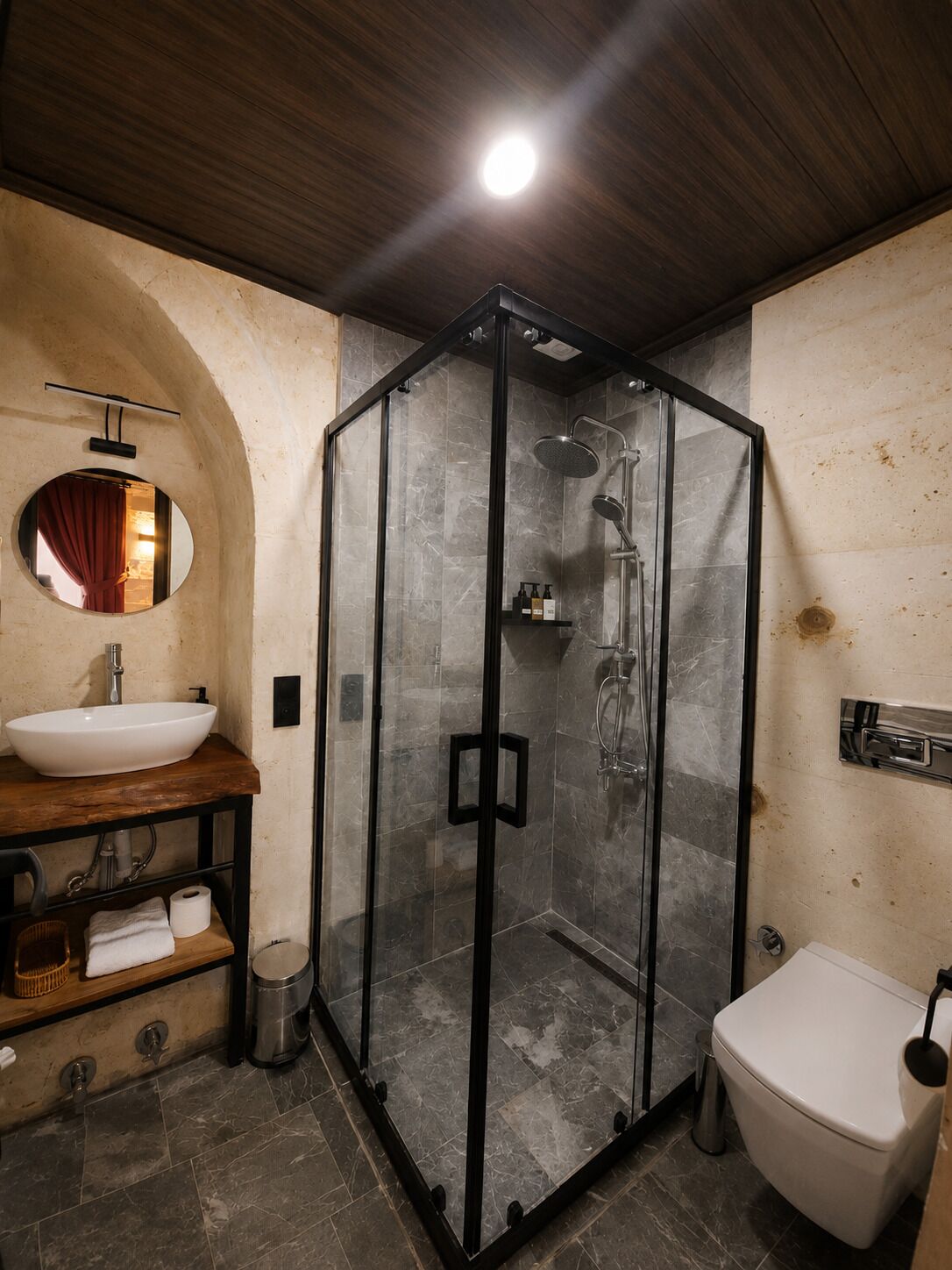 Un baño moderno con cabina de ducha de vidrio, tocador de madera con lavamanos y un inodoro.