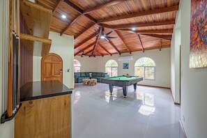 A spacious indoor area with a pool table, a wooden ceiling, and a large arched window. - Casa Vida Tropical / Your Private Oasis in the Heart of Jaco (Jacó)