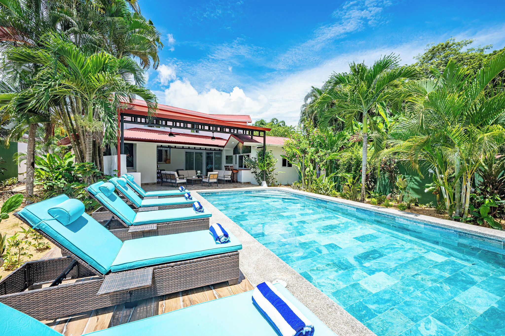 Une piscine avec des chaises longues, un patio couvert et une végétation luxuriante.