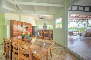 A spacious kitchen with wooden cabinets, a large dining table, and chairs. There is a view of a patio area with outdoor seating. - Casa Vida Tropical / Your Private Oasis in the Heart of Jaco (Jacó)