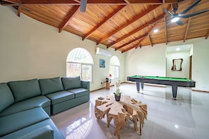 A spacious living room with a green sofa, a wooden coffee table, a pool table, and a ceiling fan. - Casa Vida Tropical / Your Private Oasis in the Heart of Jaco (Jacó)