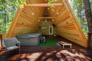 Una cabaña de madera acogedora con forma triangular, un jacuzzi, una mesita y un banco.