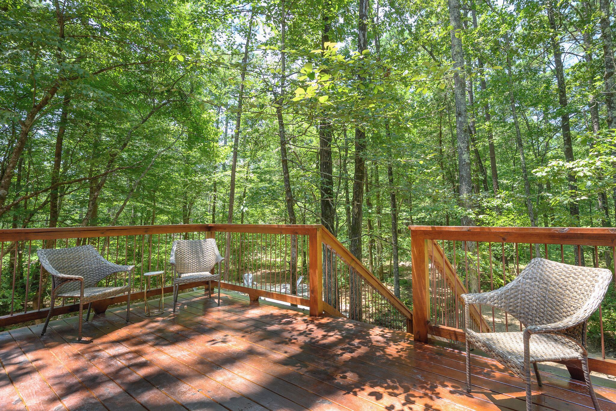 A wooden deck with wicker chairs and a railing, surrounded by a forest.