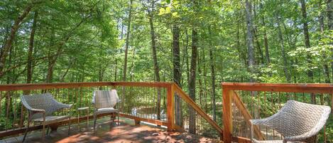 A wooden deck with wicker chairs and a railing, surrounded by a forest.