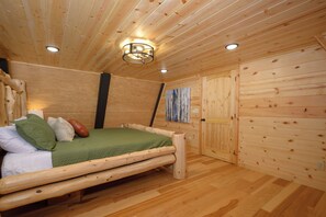 Una habitación con paneles de madera, una cama, una lámpara fijada a la pared y una puerta.