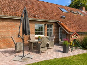 Ein Backsteinhaus mit einem Ziegeldach, einer Terrasse und Gartenmöbeln sowie einem Vogelhaus.