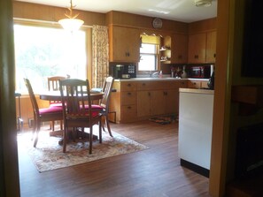 A kitchen with wooden cabinets, a dining table with chairs, a refrigerator, and a clock on the wall.
