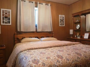 A bedroom with a wooden bed, a nightstand with a lamp, and a dresser with a mirror.