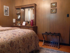 Una habitación de hotel con una cama, un aparador, un espejo y una mesita de noche con una lámpara.