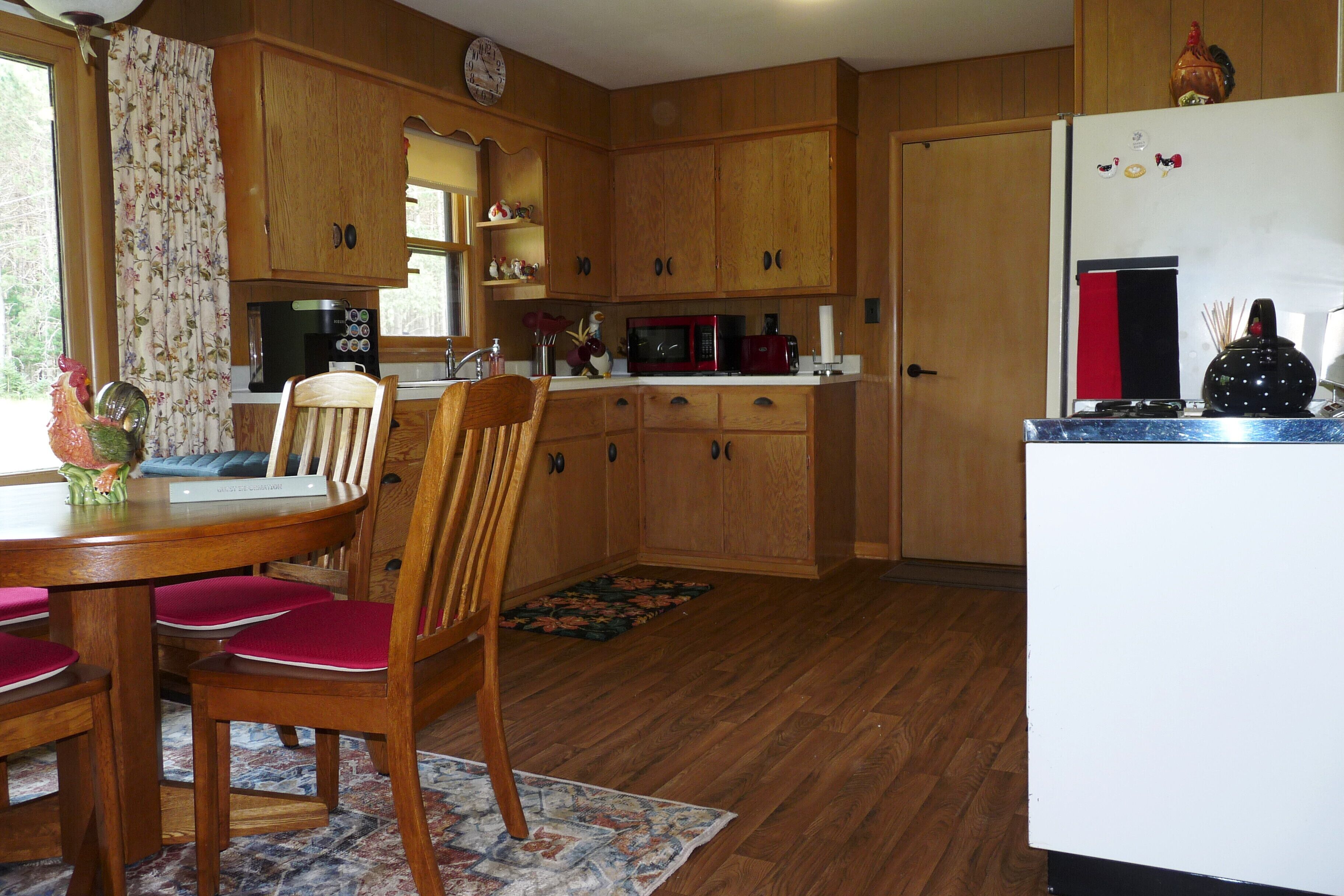 Una cocina con armarios de madera, una mesa de comedor con sillas, un refrigerador y un microondas.