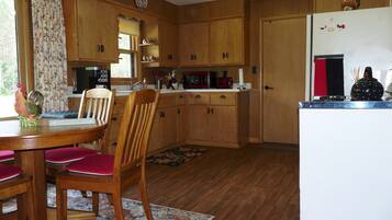 Una cocina con armarios de madera, una mesa de comedor con sillas, un refrigerador y un microondas.