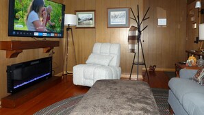Ett rum med en platt-TV som är monterad på väggen, en soffa, en fåtölj och ett litet bord med en lampa.