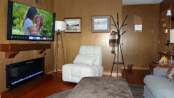 A room with a flat-screen TV mounted on the wall, a sofa, a chair, and a small table with a lamp.