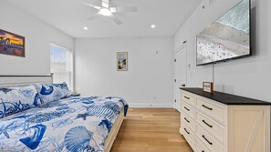 Un dormitorio con cama, cómoda, televisor y ventilador de techo.