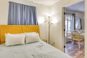 A bedroom with a wooden headboard, a bed with white bedding, a floor lamp, and a view of an outdoor dining area through an open door. - Cozy South Lake Tahoe Cabin | Near Beaches, Mountain Bike Trails & Heavenly (South Lake Tahoe)