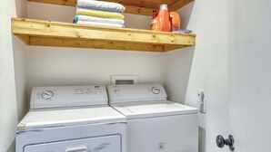 A laundry area with two stacked washers and dryers, a wooden shelf above with folded towels, and a wall-mounted power outlet. - Cozy South Lake Tahoe Cabin | Near Beaches, Mountain Bike Trails & Heavenly (South Lake Tahoe)