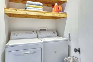Ein Waschraum mit zwei übereinander gestapelten Waschmaschinen und Trocknern, ein Holzregal darüber mit gefalteten Handtüchern und einer wandmontierten Steckdose.