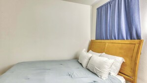 A single bed with a wooden headboard, white pillows, and a light blue bedspread in a room with plain walls and a window with blue curtains. - Cozy South Lake Tahoe Cabin | Near Beaches, Mountain Bike Trails & Heavenly (South Lake Tahoe)