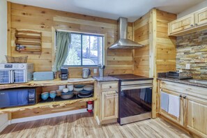 A compact kitchen with wooden walls, a window, and built-in appliances. - Cozy South Lake Tahoe Cabin | Near Beaches, Mountain Bike Trails & Heavenly (South Lake Tahoe)