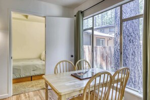 A room with a dining table, four chairs, a bench, and a window with a view of a wooden fence and trees. - Cozy South Lake Tahoe Cabin | Near Beaches, Mountain Bike Trails & Heavenly (South Lake Tahoe)