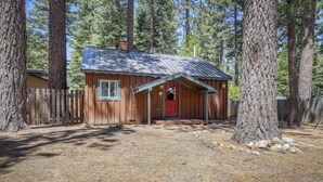 A small wooden cabin with a red door, surrounded by tall trees and a wooden fence. - Cozy South Lake Tahoe Cabin | Near Beaches, Mountain Bike Trails & Heavenly (South Lake Tahoe)