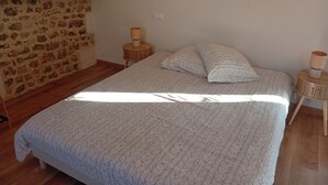 Een slaapkamer met een stenen muur, een houten bedframe, een bedlampje en een klein rond tafeltje.